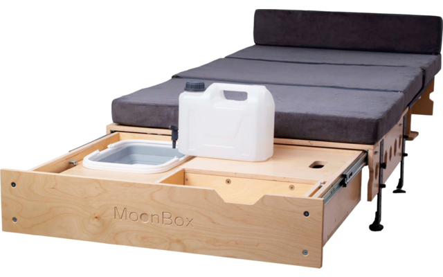 Ausgezogene Holzschublade mit der Aufschrift "MoonBox", darauf ein weißer Kanister und ein graues Faltbecken, dahinter eine graue gepolsterte Liegefläche mit Kopfstütze und schwarzen Beinen
