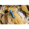 Blaue Trinkflasche mit weißer Aufschrift liegt auf einem nassen Felsen, Wasser fließt daneben