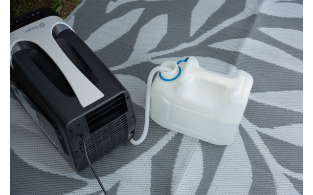Mobiele airconditioner links met zwart-witte behuizing; een witte afvoerslang loopt naar een rechthoekige, doorschijnende witte watercontainer met blauwe schroefdop; apparaat en container staan op een grijze mat met een licht bladmotief