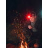 Person hockt neben einem Lagerfeuer mit Funkenflug nachts