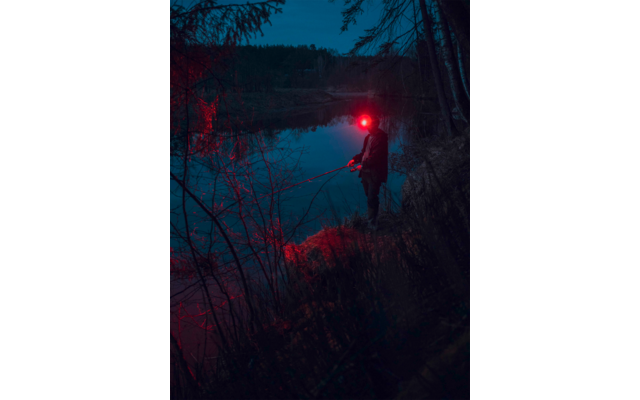 Person mit rotem Licht am Ufer eines Sees bei Nacht