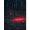 Person mit Taschenlampe in dunklem Wald, rotes Licht auf dem Waldboden