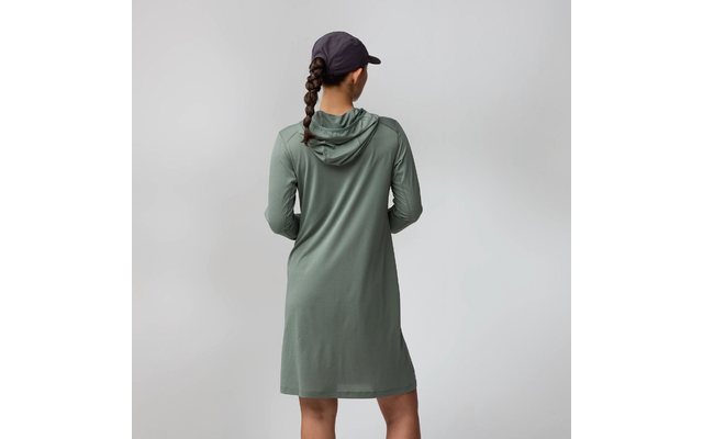 Personne vue de dos, cheveux tressés, portant une robe à capuche verte et une casquette noire sur fond gris clair