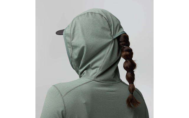 Vue de dos d'une personne portant une veste à capuche verte, capuche relevée, la visière d'une casquette dépasse, longue queue de cheval segmentée par plusieurs élastiques