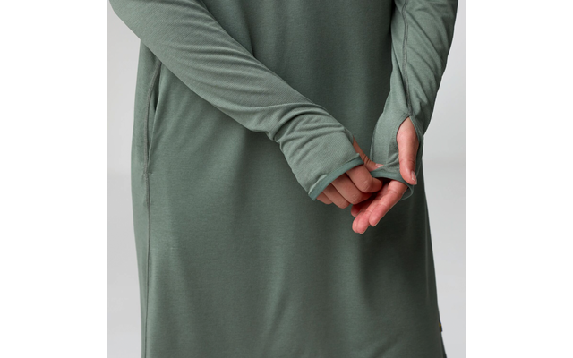 Buste et mains d'une personne portant un vêtement vert à manches longues avec ouvertures pour le pouce, mains derrière le dos, fond clair