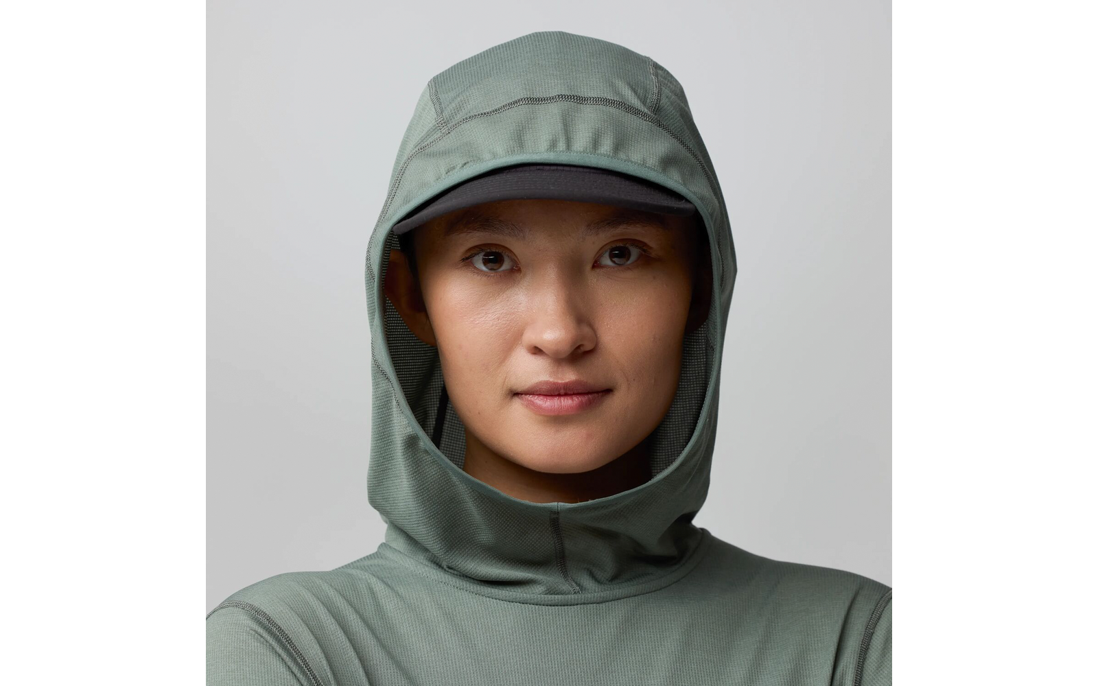 Personne face à l'appareil, visage visible, porte une capuche verte et une casquette sombre