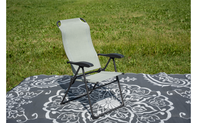 Sedia pieghevole verde chiaro con braccioli su un tappeto grigio con motivo floreale bianco, prato sullo sfondo