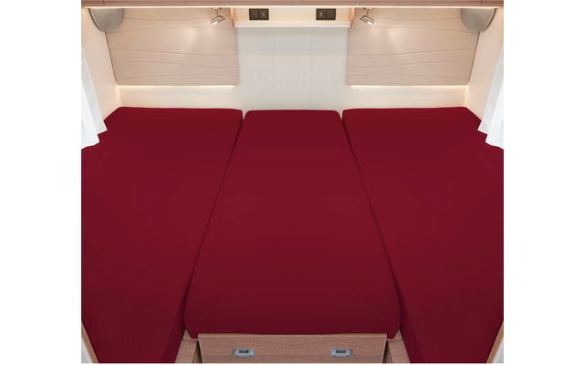 Trois lits côte à côte avec des draps rouges dans une pièce lumineuse