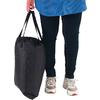 Unterkörper einer Person mit blauem Oberteilsaum, dunkler Hose und Sneakers, Hand hält eine schwarze Tasche seitlich