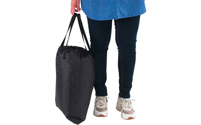 Unterkörper einer Person mit blauem Oberteilsaum, dunkler Hose und Sneakers, Hand hält eine schwarze Tasche seitlich
