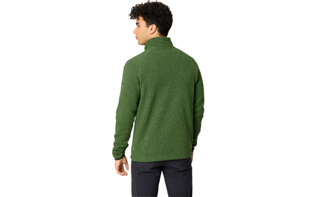 Person steht mit dem Rücken zur Kamera, trägt grünen Pullover mit Stehkragen und dunkle Hose, Kopf nach links gedreht