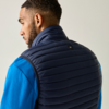 Persoon van achteren, hoofd zijwaarts gedraaid, draagt een donkerblauwe gewatteerde bodywarmer over een blauw fleece trui