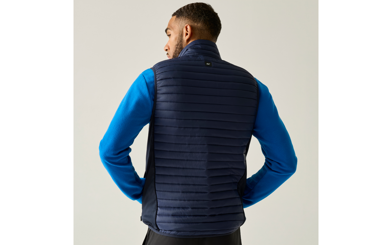 Persoon van achteren in donkerblauwe gewatteerde bodywarmer over blauw longsleeve-shirt tegen lichte achtergrond