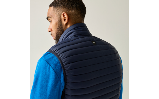 Persoon van achteren, hoofd zijwaarts gedraaid, draagt een donkerblauwe gewatteerde bodywarmer over een blauw fleece trui