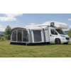 Camper bianco con veranda montata con grandi finestre trasparenti, su un prato, alberi e cielo azzurro sullo sfondo