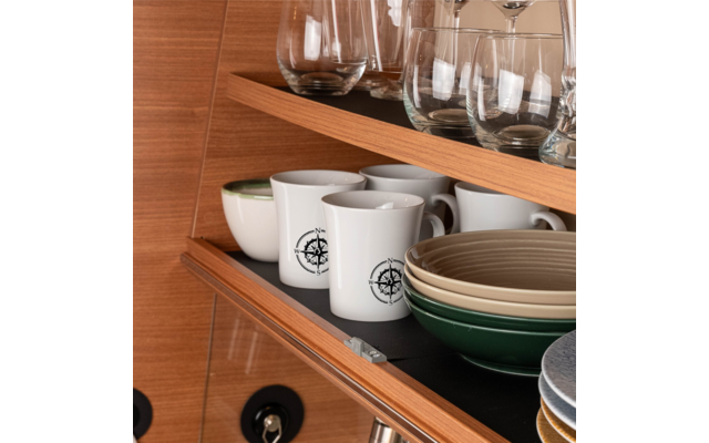 Holzschrankfach mit oben stielosen Gläsern, weißen Tassen mit schwarzem Logo und gestapelten grünen und beigen Schalen sowie Tellern