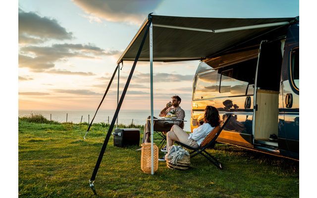 Two people sitting on camping chairs next to a camper van at sunset
