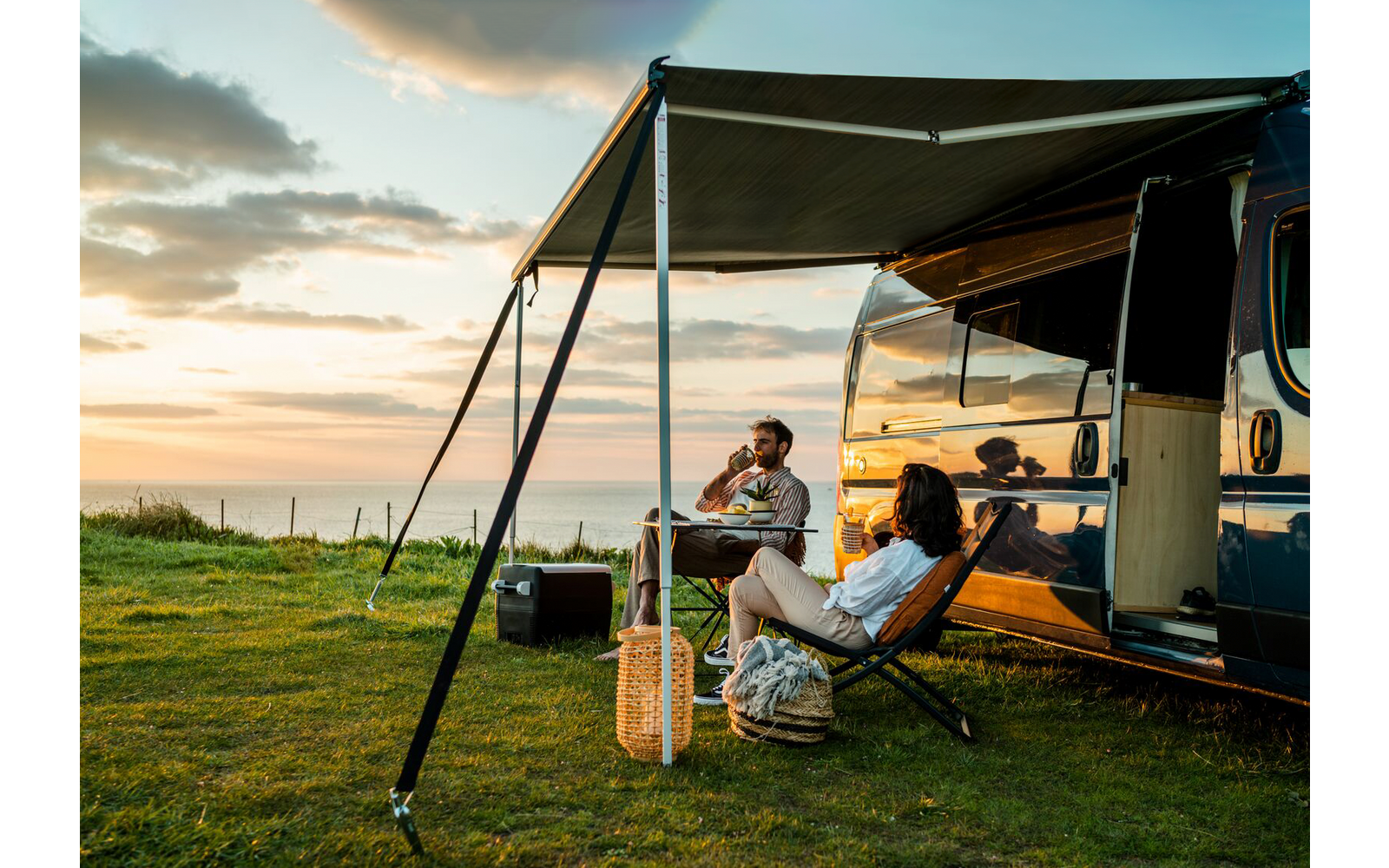 Two people sitting on camping chairs next to a camper van at sunset