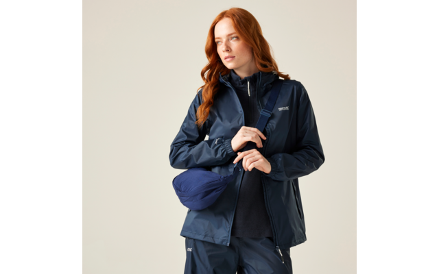 Person mit roten, welligen Haaren in dunkelblauer Regenjacke, dunkler Hose und blauer Umhängetasche, schaut nach rechts