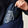 Hand steckt dunkelblaue, in Beutel verpackte Regatta-Jacke mit Aufdruck "Regatta Great Outdoors" und "Women's Pack-It Jacket Waterproof & Breathable 10/S" in eine offene dunkelblaue Reißverschlusstasche
