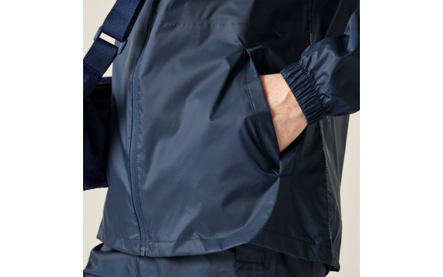 Primo piano del busto con giacca antipioggia blu scuro, mano destra nella tasca laterale, tracolla visibile