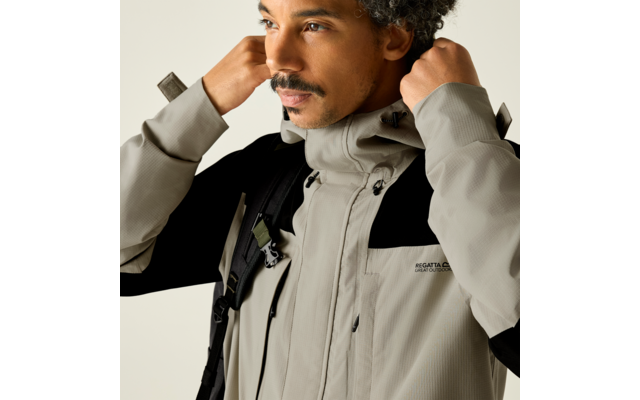 Nahaufnahme einer Person, die den Kragen einer hellgrauen Outdoorjacke mit Reißverschlüssen anfasst; Rucksackträger sichtbar