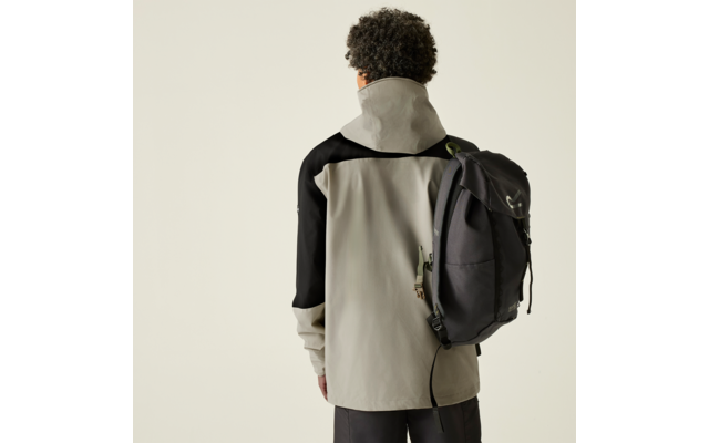 Person von hinten, trägt hellgraue Jacke mit schwarzen Ärmeln und einen schwarzen Rucksack über einer Schulter, dunkle lockige Haare, einfarbiger heller Hintergrund