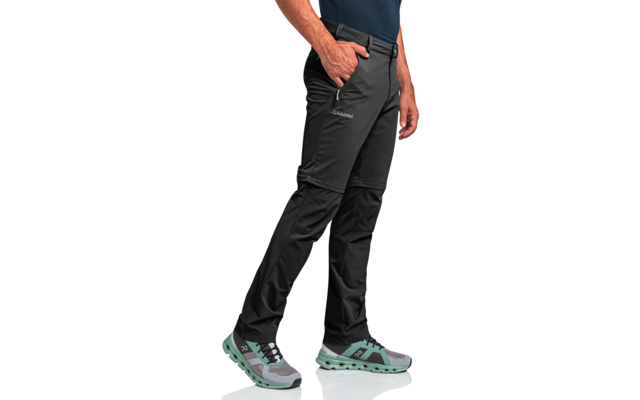 Bein- und Hüftbereich einer stehenden Person mit schwarzer Zip-off-Outdoorhose, rechte Hand in Hosentasche und graugrünen Trekkingschuhen