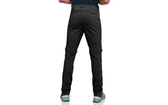 Rückenansicht einer stehenden Person mit schwarzer Hose und hellgrünen Sportschuhen vor weißem Hintergrund