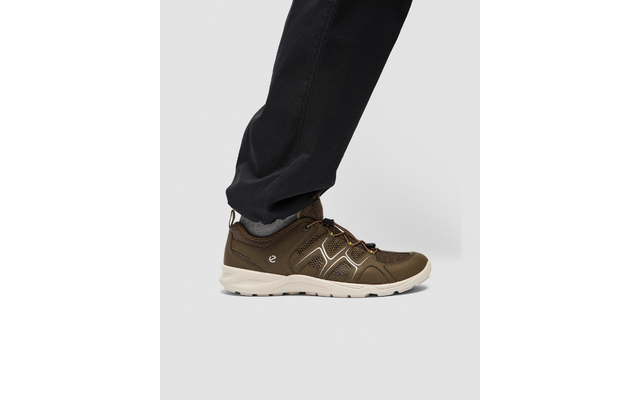 Vista lateral de un pie derecho con un zapato con cordones marrón y suela beige claro, calcetín gris y pantalón oscuro sobre fondo gris claro