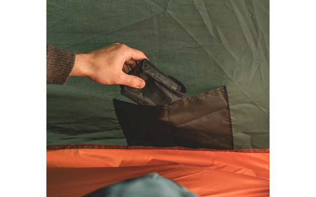 Hand legt schwarzen Gegenstand in grüne Tasche auf einem Bett