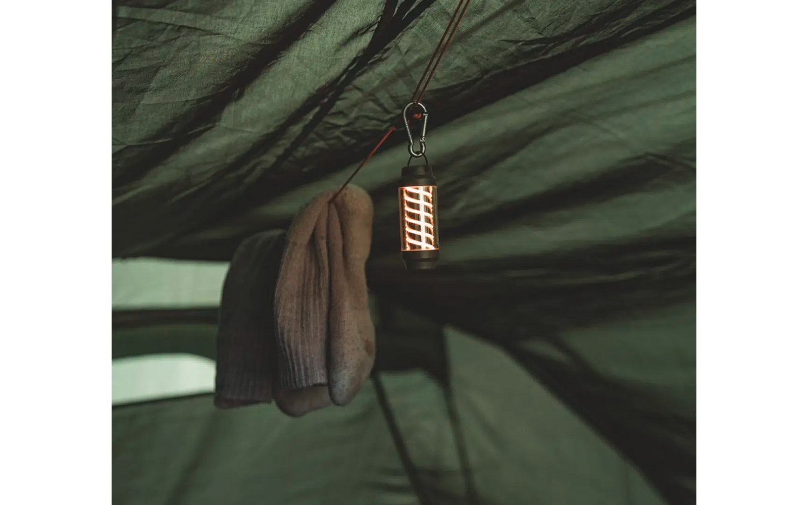 Eine braune Jacke hängt an einem Haken an einer Zeltdecke aus grünem Stoff