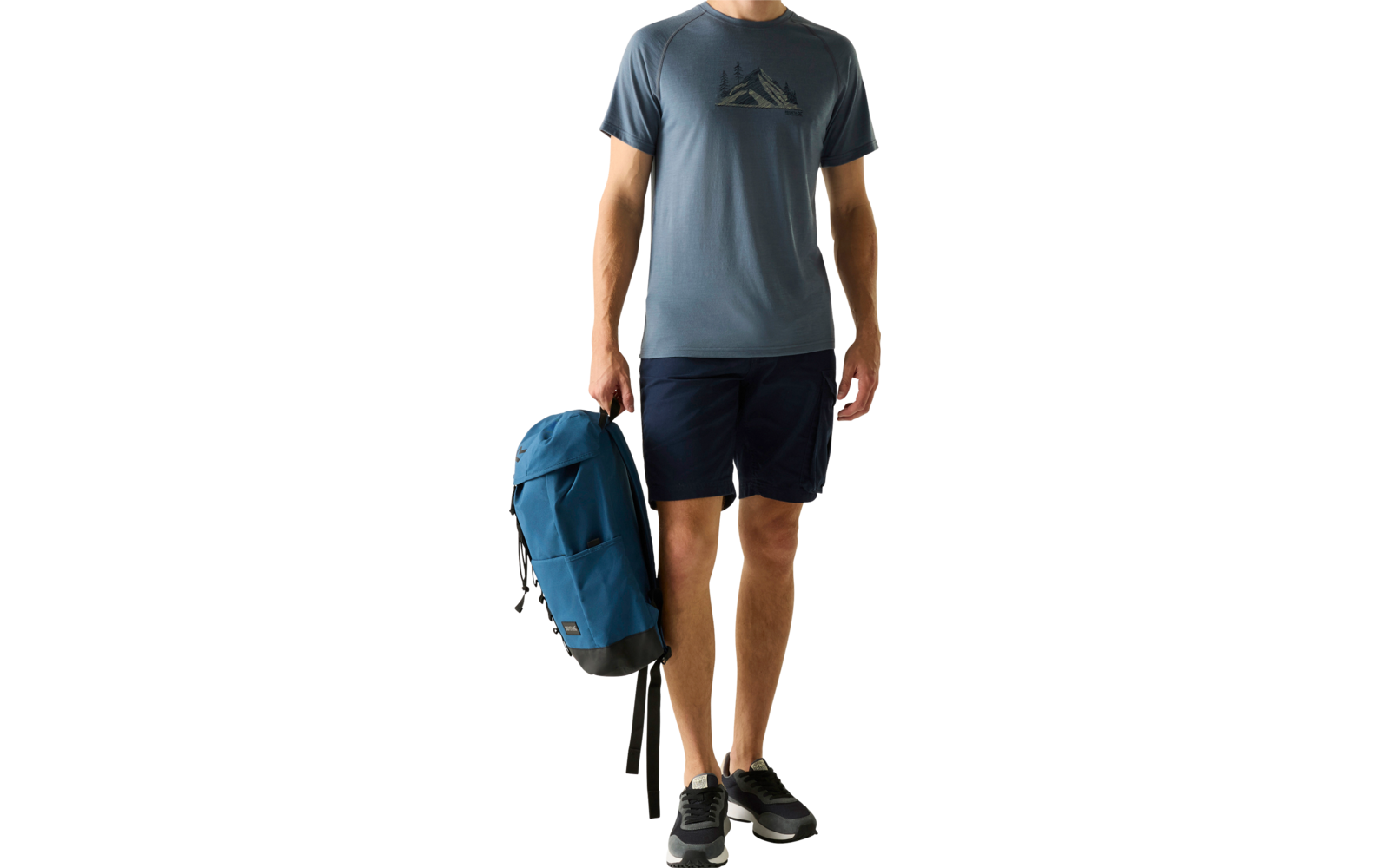 Mann steht, hält blauen Rucksack in der rechten Hand, trägt blaues T‑Shirt mit Bergmotiv, dunkle Shorts und schwarze Sneaker vor hellem einfarbigem Hintergrund