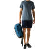 Mann steht, hält blauen Rucksack in der rechten Hand, trägt blaues T‑Shirt mit Bergmotiv, dunkle Shorts und schwarze Sneaker vor hellem einfarbigem Hintergrund