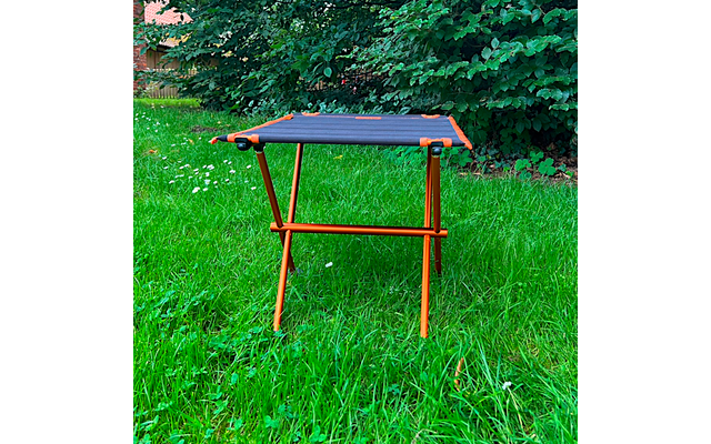 Oranje metalen frame met zwart rechthoekig doek, vier poten, op groen gras voor struiken