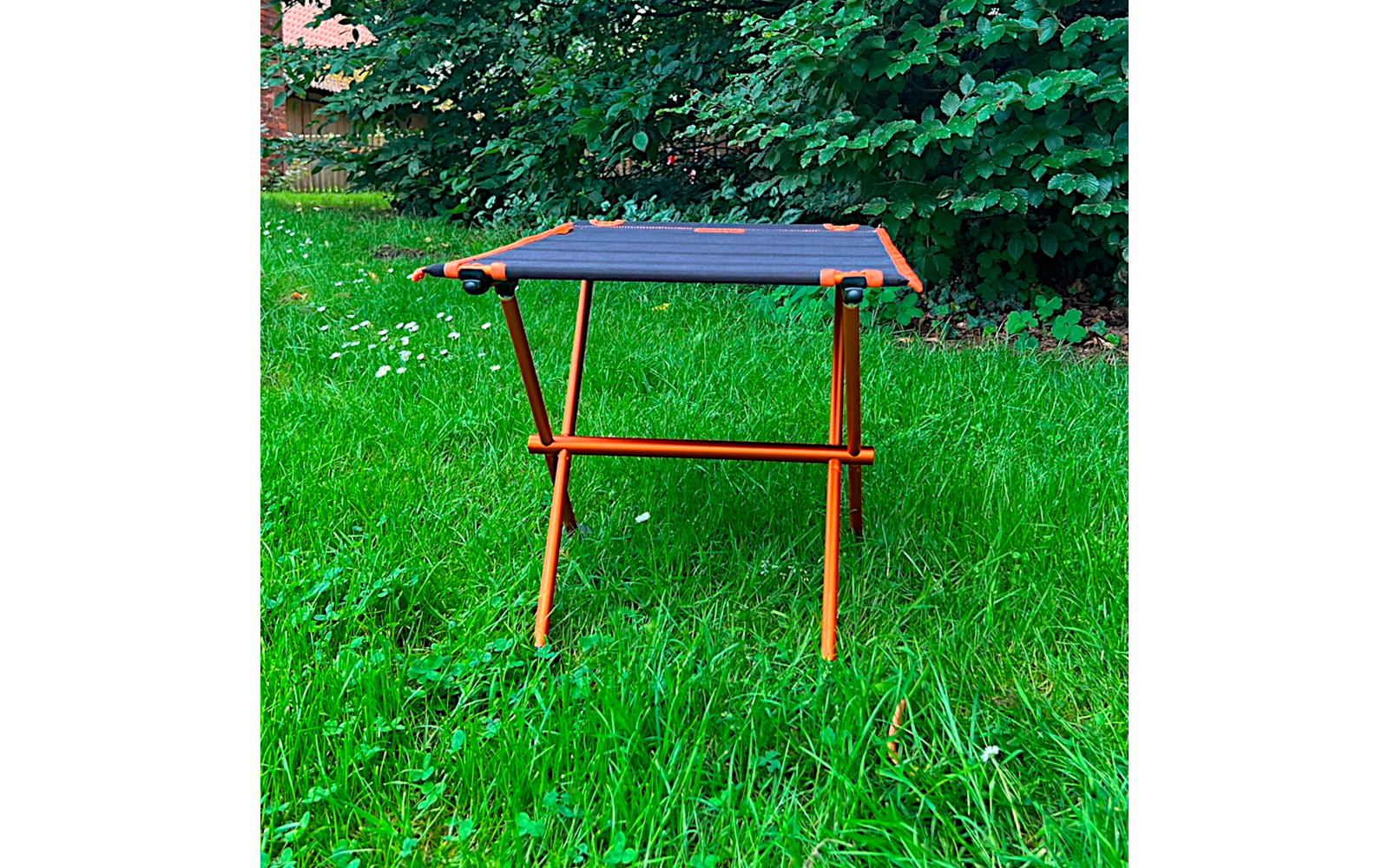 Oranje metalen frame met zwart rechthoekig doek, vier poten, op groen gras voor struiken