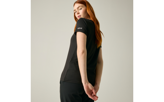 Persona con capelli rossi in posizione leggermente di tre quarti, indossa una t‑shirt nera, guarda oltre la spalla, mani dietro la schiena, sfondo chiaro uniforme