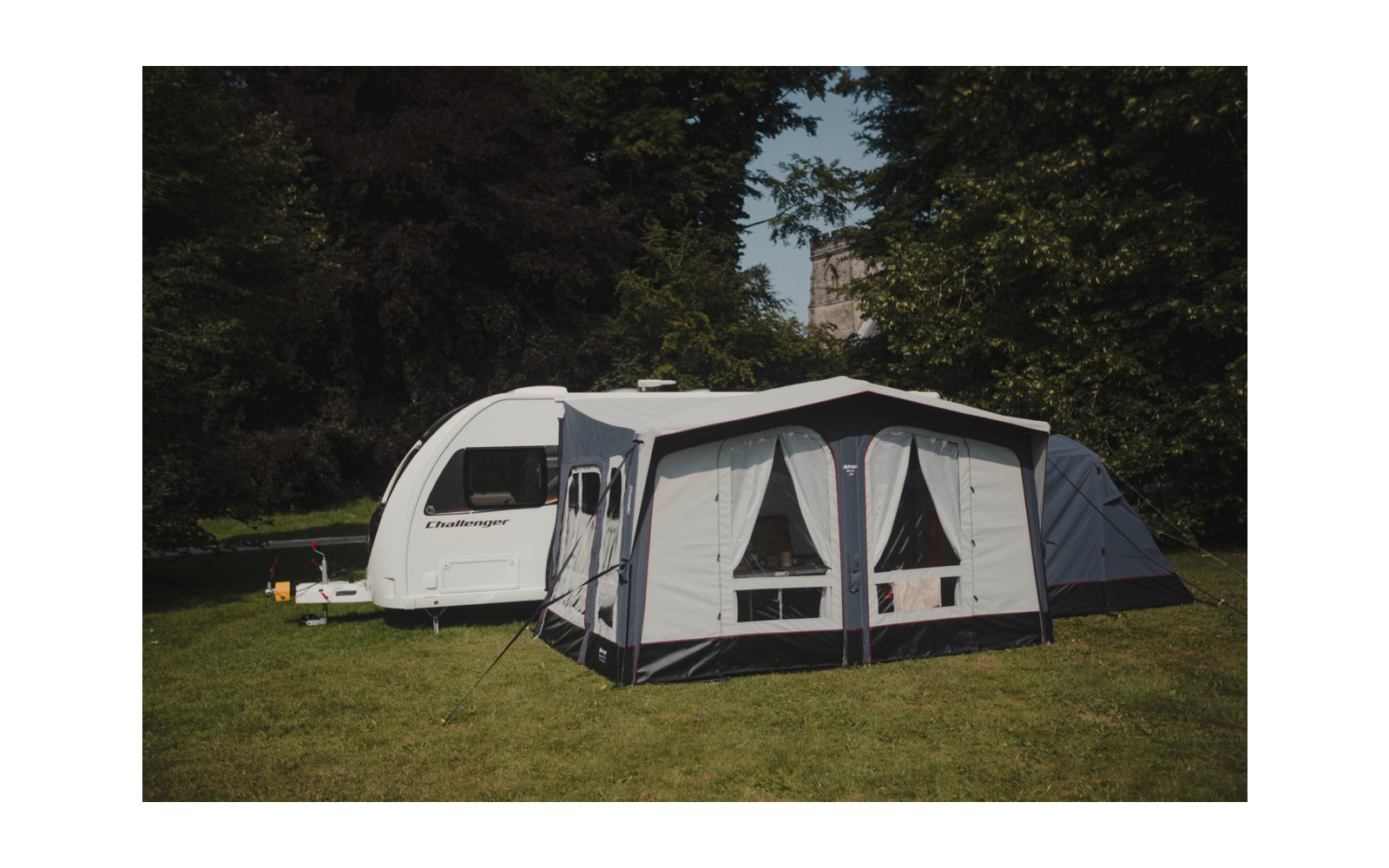 Una caravana con un toldo adjunto está sobre un césped, rodeada de árboles