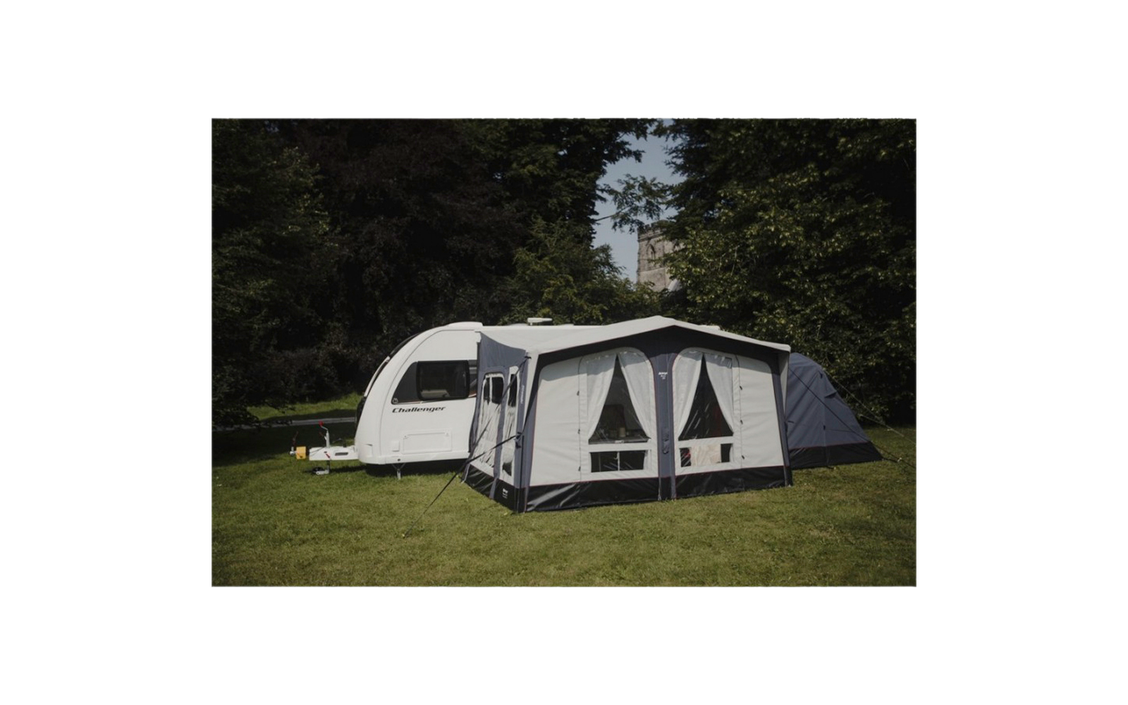 Caravana con toldo adjunto en un área de césped, rodeada de árboles