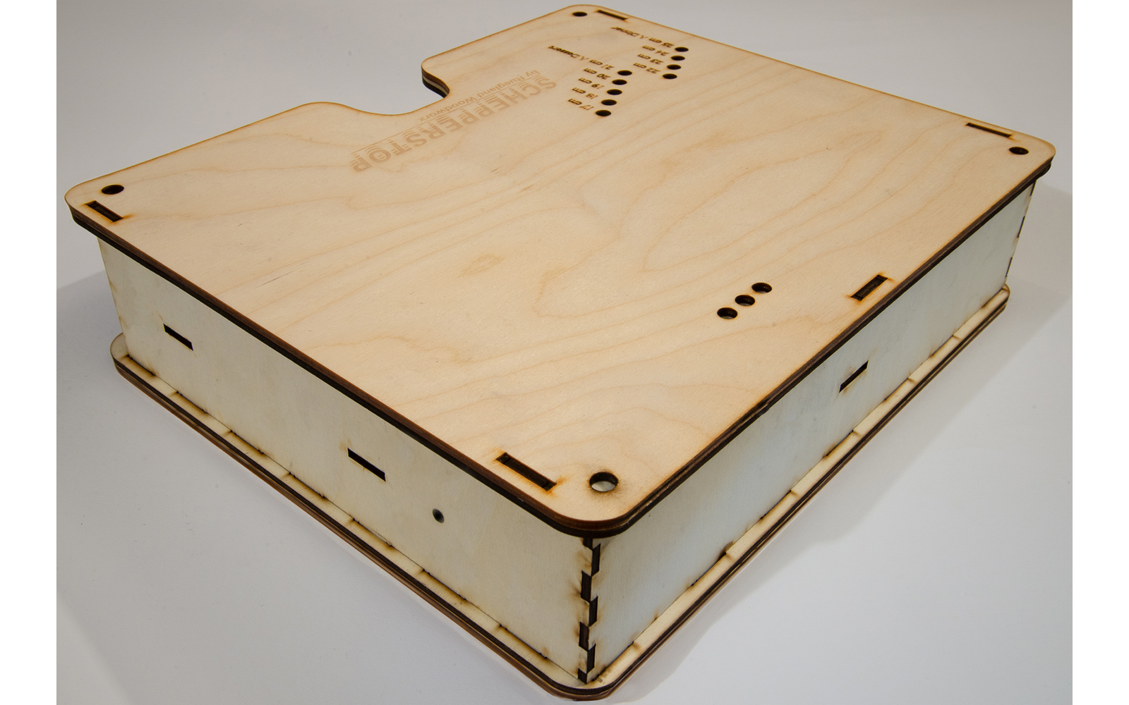 Flat square wooden box of light plywood with slots, round holes and visible interlocking joints at the edges