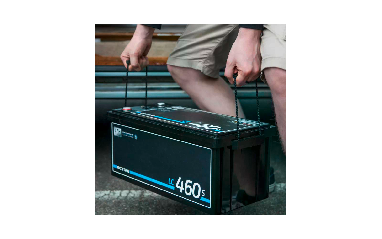 Person hebt eine schwarze Autobatterie mit beiden Händen