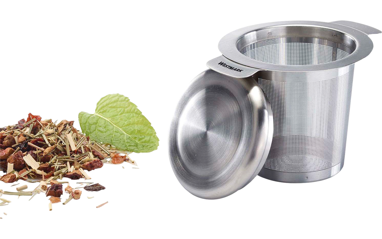 Infuseur à thé en acier inoxydable avec couvercle à côté de feuilles de thé en vrac et d'une feuille de menthe sur fond blanc