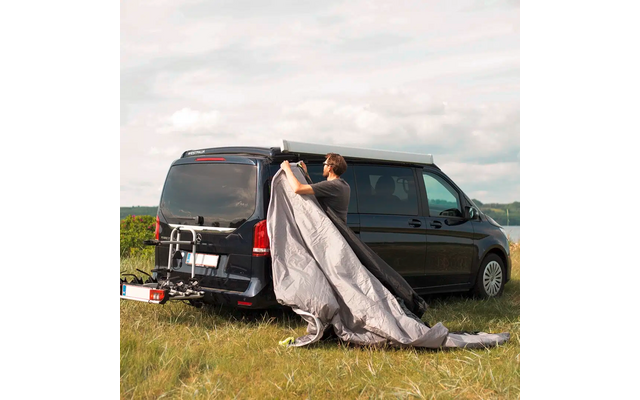 Person breitet eine Decke hinter einem schwarzen Van auf einer Wiese aus