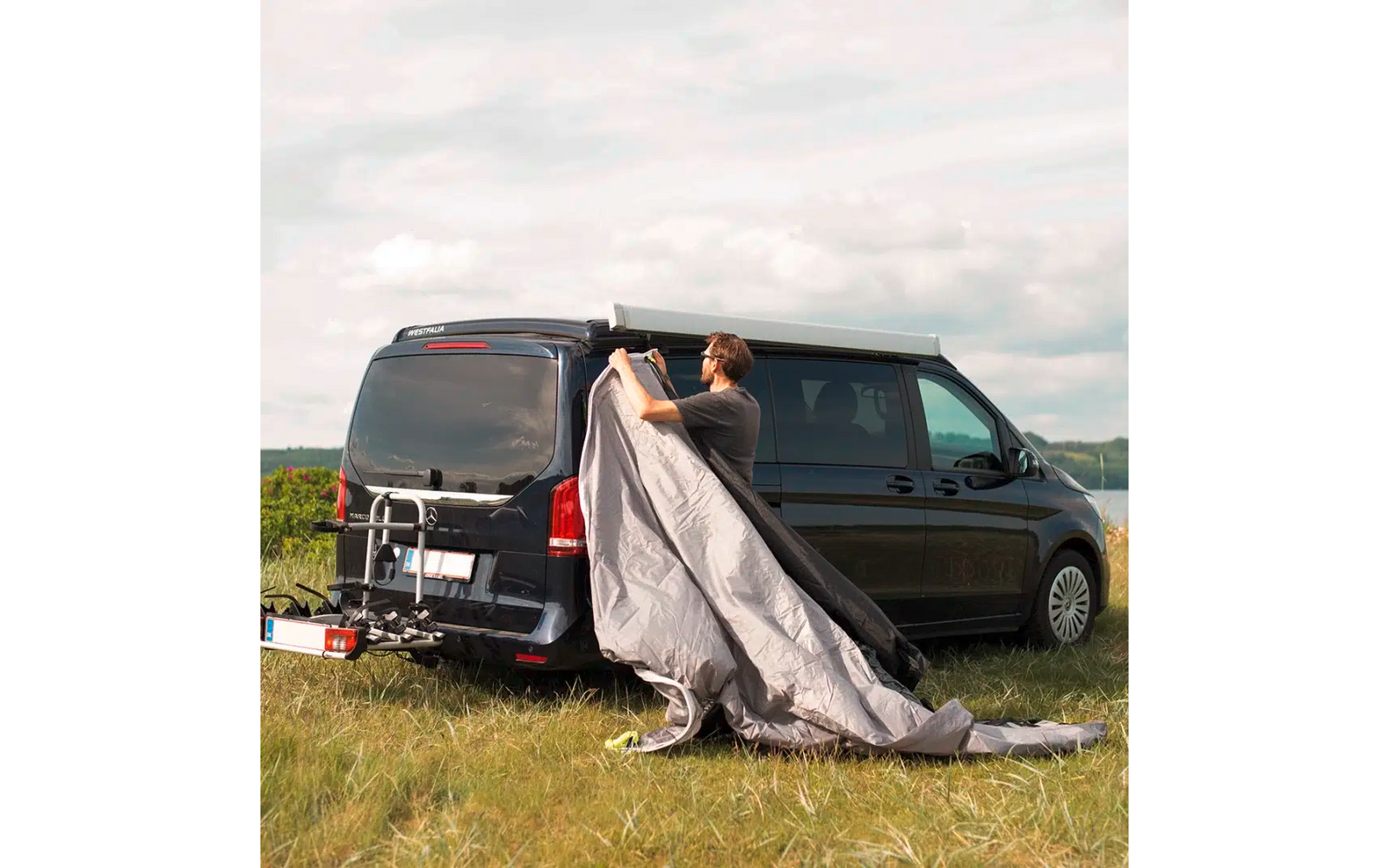 Person breitet eine Decke hinter einem schwarzen Van auf einer Wiese aus