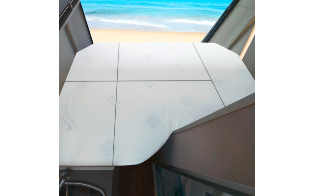 Weiße mehrteilige Fläche mit sichtbaren Nähten vor offenem Fenster; im Hintergrund Sandstrand und Meer; links Metallfuß, rechts Ränder einer Sitzbank