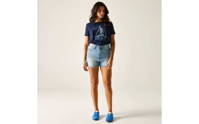Person steht auf hellem Hintergrund, trägt dunkelblaues T‑Shirt mit Segelboot‑Print, hellblaue Jeans‑Shorts, blaue Sneakers und ein Armband am linken Handgelenk