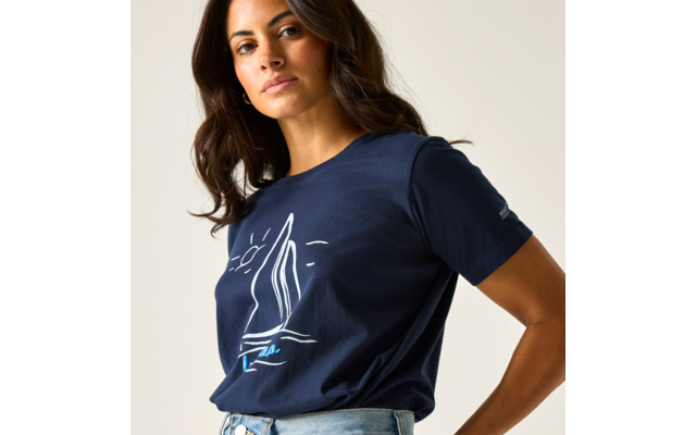 Frau mit schulterlangem dunklem Haar, trägt dunkelblaues T‑Shirt mit weißem Segelboot-Print und helle Jeans