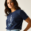 Frau mit schulterlangem dunklem Haar, trägt dunkelblaues T‑Shirt mit weißem Segelboot-Print und helle Jeans