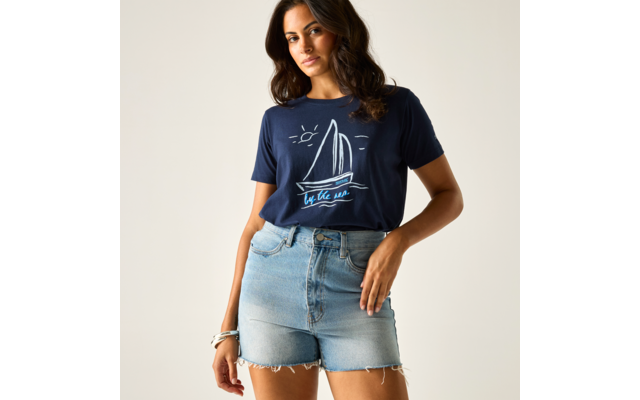 Person mit dunkelblauem T‑Shirt mit Segelboot‑Aufdruck und hellen Jeansshorts vor hellem Hintergrund