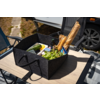 Schwarze Filztasche auf einem Holztisch mit zwei Baguettes in Papier, Kopfsalat, zwei Zucchini, gelber Butterdose, Flasche und blau-weiß kariertem Tuch; im Hintergrund Wohnwagen und Autoreifen